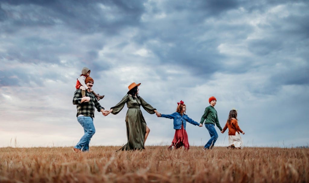 Family Photographer, a family of six walk hand in hand through a dry meadow